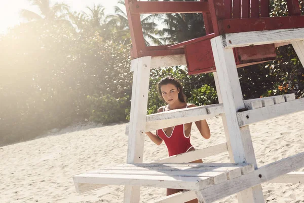 Donna sexy in costume da bagno rosso accanto alla torre del bagnino sulla spiaggia — Foto Stock