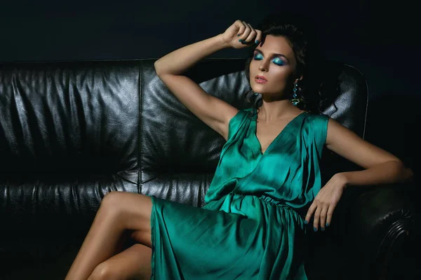 性感的女人在美丽的绿色礼服在皮革沙发上摆姿势 — 图库照片