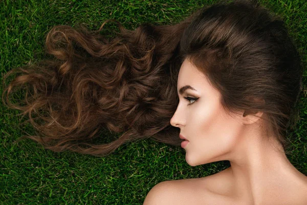 Mulher bonita com um cabelo encaracolado saudável está deitado na grama — Fotografia de Stock