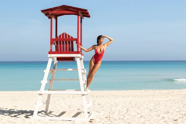 Femme sexy en maillot de bain rouge posant à côté d'une tour de sauveteur — Photo