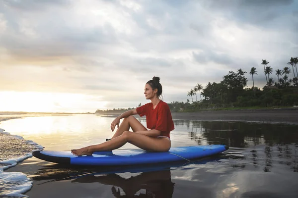 Mulher sentada na prancha de surf na praia depois de sua sessão de surf — Fotografia de Stock