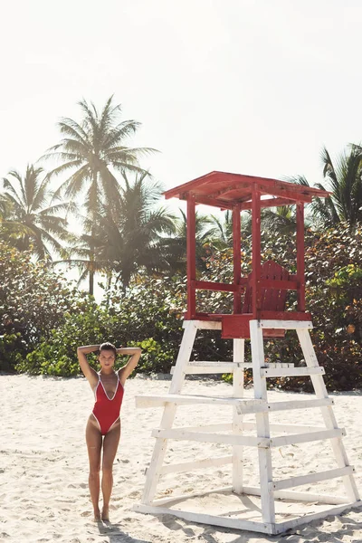 Mulher sexy em maiô vermelho ao lado da torre de salva-vidas na praia — Fotografia de Stock