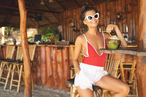 Mujer joven y sexy sentada en un auténtico bar de playa con un cocon —  Fotos de Stock