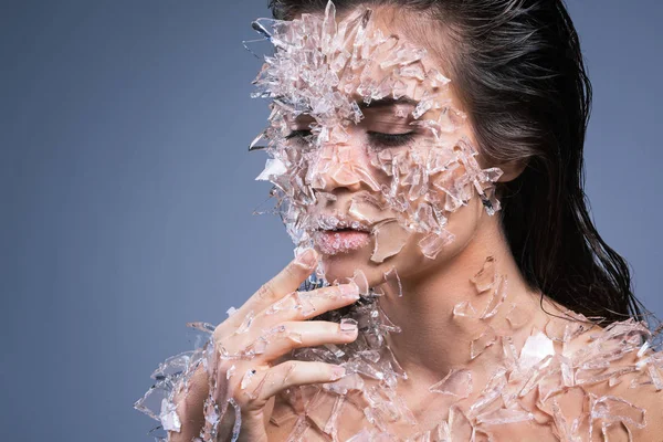 Female face covered with a lot small pieces of glass or ice