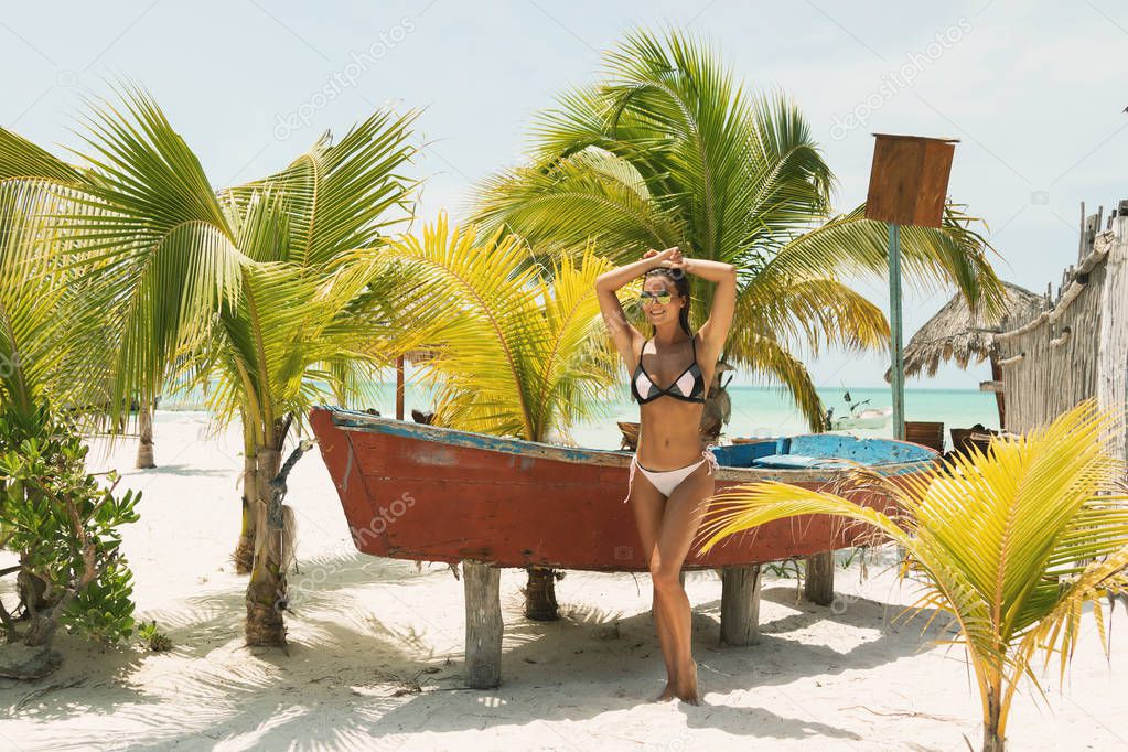 Beautiful woman wearing bikini and sunglasses beside a old boat