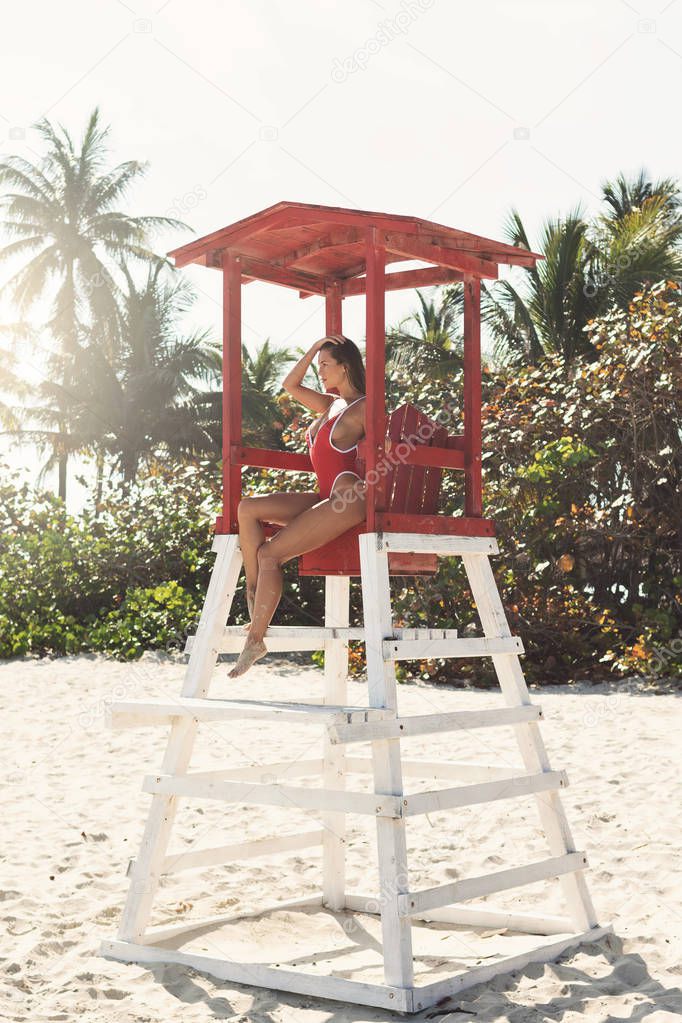 Sexy woman in red swimsuit beside lifeguard tower on the beach