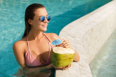 Mutlu kadın yüzme havuzunda dinleniyor ve hindistan cevizi suyu içiyor.