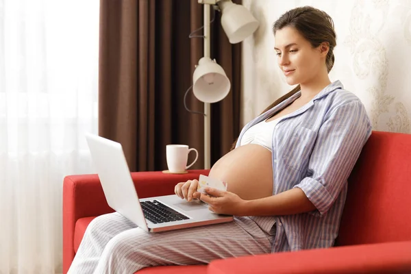 Genç ve güzel hamile bir kadın kredi kartıyla online alışveriş yapıyor. 