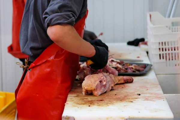 Slager in rode schort het hakken van vlees van pluimvee op teller van snijden winkel op boerderij markt. — Stockfoto