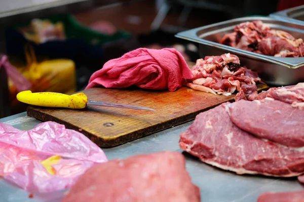 Contador del vendedor de carne fresca en el mercado de agricultores locales. Tabla de cortar de madera, cuchillo, trapo rojo, cerdo, carne de res, contenedor con desechos . — Foto de Stock