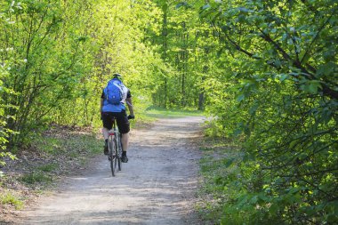 Adam bisikletçi koruyucu, dişli e-park sokakta birçok ağaçları arasında yaz gününde Bisiklete binmek. Arkadan görünüm.