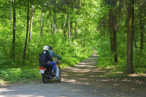 Young couple riding motorcycle in tunnel of trees in forest.