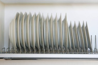 Modern mutfak kurutma sofra için raf. Temiz, beyaz cam ve metal raf üzerinde seramik yemekleri Mutfak dolap içinde yıkanmış.