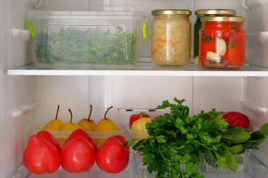 Açık buzdolabı. Sağlıklı taze gıda armut, maydanoz, salatalık, domates, biber. Kavanoz ve buzdolabı rafta sebze konserveler.