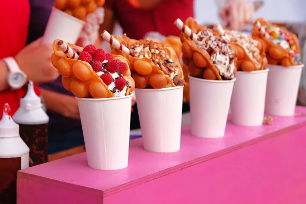 Kabarcık waffle ahududu, çikolata ve şekerleme beyaz kağıt bardak ile açık mutfak gıda festival olay üzerinde satılmaktadır. Gıda ahır sokak gıda.