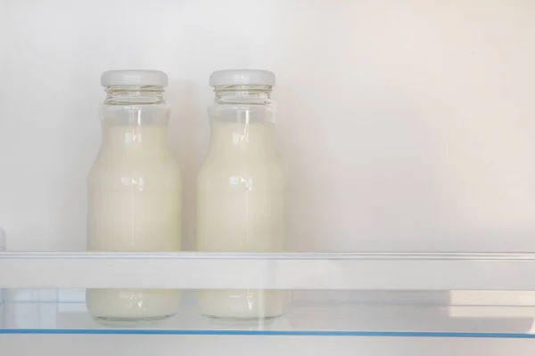 Dairy products in glass bottles on shelf of open empty fridge. White milk in  refrigerator. Horizontal view with copy space.