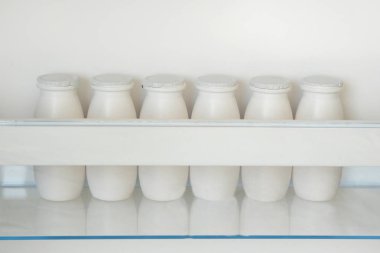 White bottles of yoghurt on shelf of open empty fridge. Weight loss diet concept. Horizontal view.