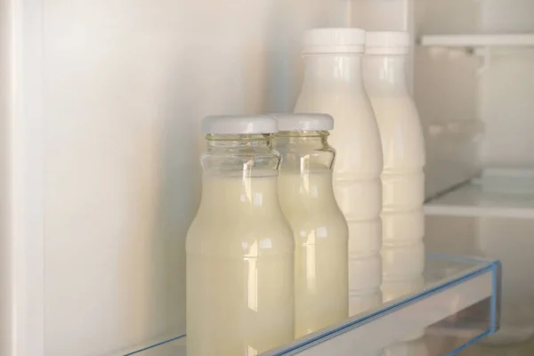 Yogurt in glass and white plastic bottles on shelf of open empty fridge. Healthy food concept. Fermented food.