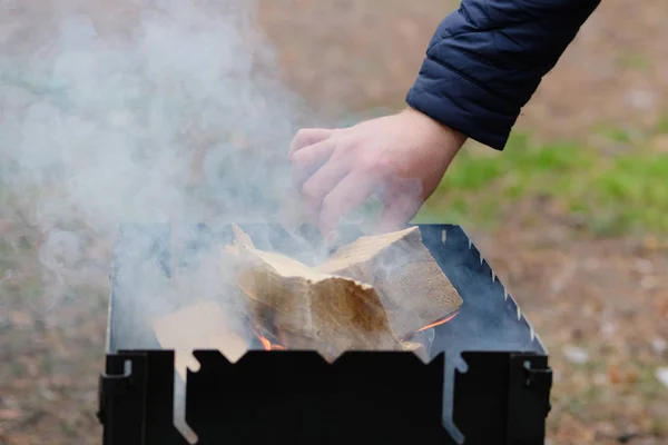 Anzünden des Grills. Seine Hand gießt Holz ins Feuer. Grillen im Wald. — Stockfoto