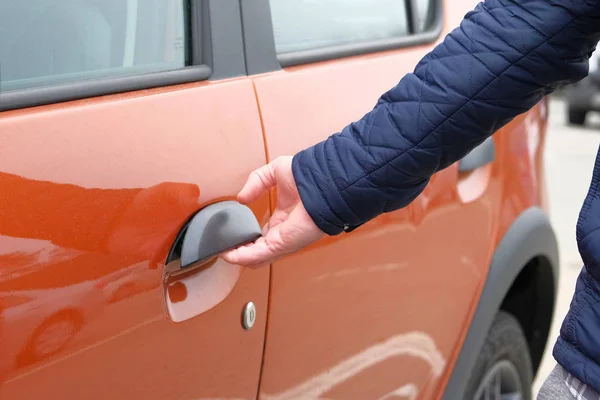 L'uomo apre la porta della sua auto arancione nel parcheggio. Mano sulla maniglia. Da vicino. . — Foto Stock