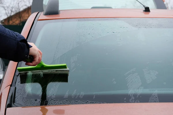 Un uomo che pulisce la sua auto arancione con lo straccio verde. Pulizia parabrezza o parabrezza mentre autolavaggio . — Foto Stock