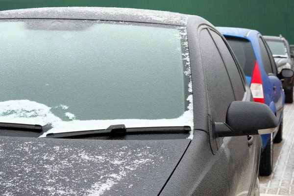 Icing on auto. Windshield in ice and snow. Cars are parked in winter.