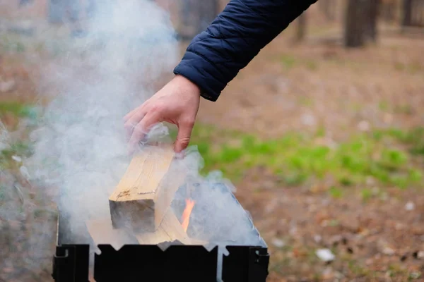 Grill mit Brennstoff und Holzkohle. Die Hand des Menschen gießt Holz ins Feuer. Grillen im Wald. — Stockfoto