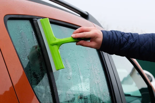 Cleaning orange car window. Washing automobile window with green mop. Drops on glass.