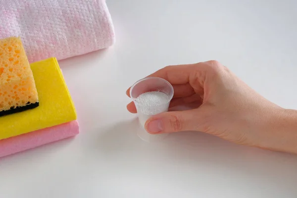 Il concetto di pulizia. Detergente per camera di pulizia. Tenere in mano un misurino di plastica con detergente granulare e salviette di stoffa. faccende di casalinga . — Foto Stock