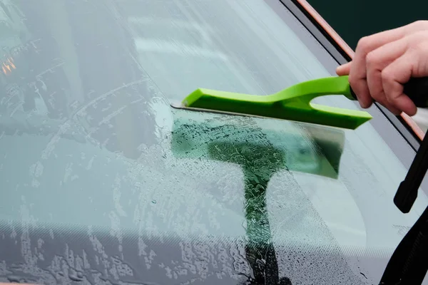 Car windows cleaning. Hand washing orange car window with green mop. Drops on glass. Close up.