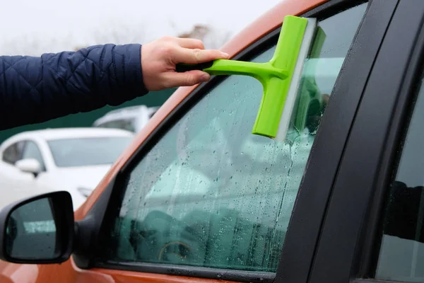 Cleaning orange car window. Washing automobile window with green mop. Horizontal view.