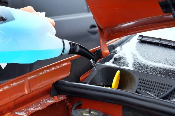 Automobile maintenance concept. Filling blue windshield washer fluid on car in winter. Close up.