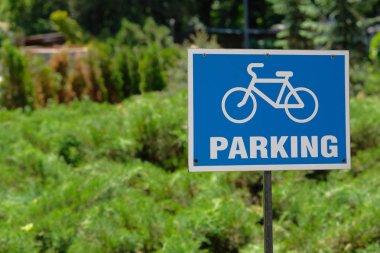 Bisiklet park yeşil ağaçların arka plan üzerinde park belirtisi. Metalik Mavi plaka üzerinde otopark yazıt. Kopya alanı.