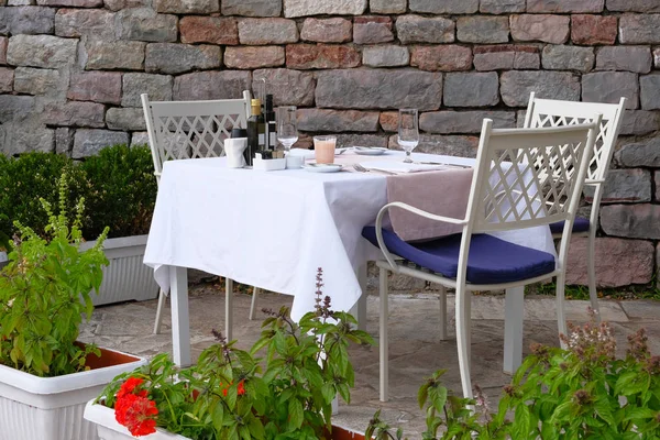 Tisch mit weißer Tischdecke, Besteck und Weingläsern auf der Sommerterrasse des Restaurants. Wand aus alten strukturierten Stein im Hintergrund. — Stockfoto