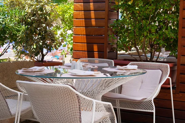 Tisch mit weißer Tischdecke, Besteck und Textilservietten auf der Sommerterrasse des Restaurants. grüne Pflanzen in Töpfen im Hintergrund. — Stockfoto