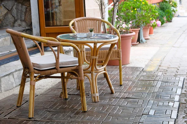 Ротанговый стол и стулья на открытой летней веранде кофейни. Цветочные горшки с зелеными растениями на заднем плане . — стоковое фото