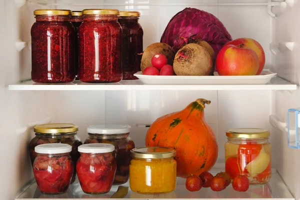 Frascos com compotas caseiras de frutas e bagas e legumes e frutas frescos vermelhos, roxos e laranja na prateleira do frigorífico. Conceito de alimentos vegetarianos saudáveis fermentados . — Fotografia de Stock