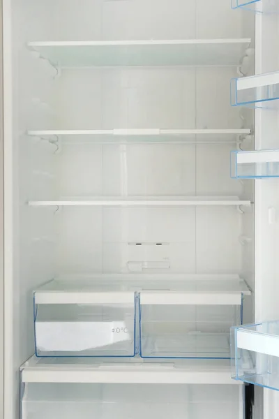 Empty white shelves in refrigerator. Diet and hunger concept. Vertical image.