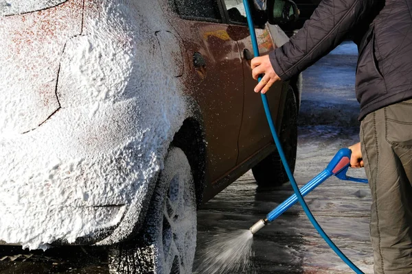 Man washes his orange car at car wash. Cleaning with soap suds at self-service car wash.