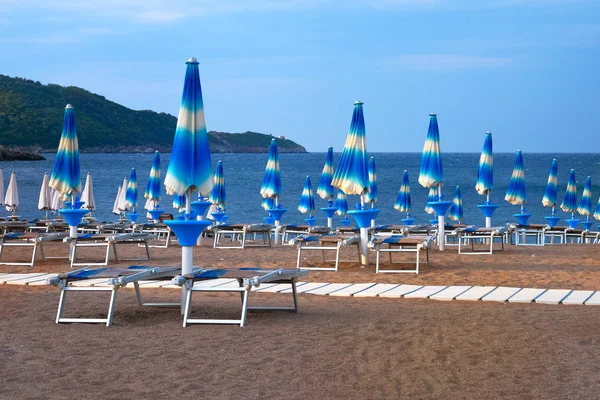 Rows of closed umbrellas and loungers on beach. Happy summer vacations concept. Paid service on beaches. — Stock Photo, Image