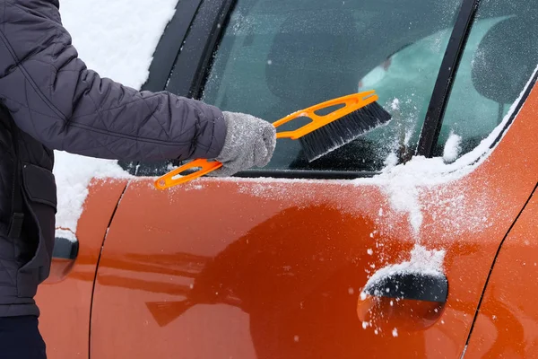 Car covered with snow. Man brushing and shoveling snow off car after snow storm. Brush in mans hand.