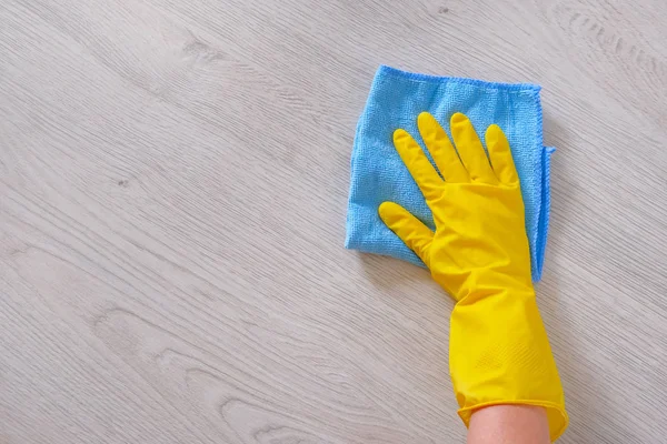 Commercial cleaning company concept. Hand in rubber protective glove with blue microfiber cloth is wiping wooden floor. Copy space.