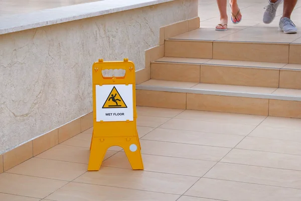 Yellow sign warning about wet floor. Inscription in plate wet floor. Steps on street near hotel.