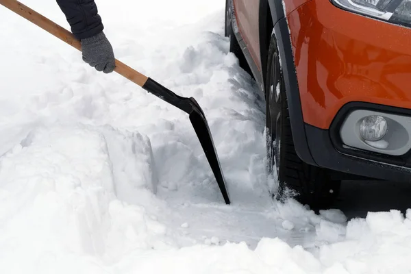 Człowiek z łopatą czyści śniegu wokół samochodu na parkingu w zimie po śniegu. Łopata w rękę. Zimowe problemy kierowców samochodów. — Zdjęcie stockowe