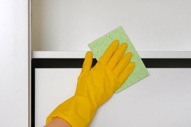 Ev hanımı evi temizler, toz temizlik bir bez ile silinerek. Sarı koruyucu eldiven elinde beyaz mobilya bez ile silerek.