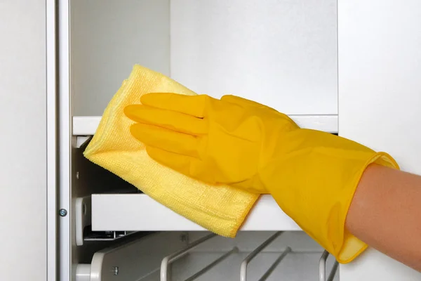 Housewife wearing protective gloves is doing housework. Hand in yellow protective glove is wiping white furniture with rag.