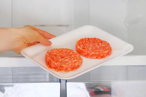Rauwe Kip Burger in container staat op plank in open koelkast. Vrouwelijke hand trekt uit de koelkast een ingrediënt voor het koken van vleesgerechten. — Stockfoto