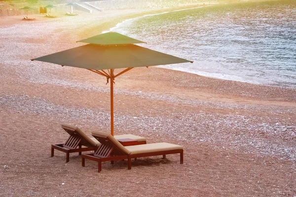 Lounge chairs with sun umbrella on beach. Comfortable vacation concept. Coastal landscape. Relaxing. Soft yellow sunlight.