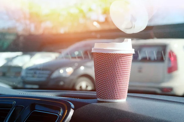 Paper cup with tea or coffee in car on sunny blurred background. Takeaway. Morning breakfast in auto.