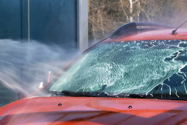 Windschutzscheibe des Autos unter mächtigem Wasserstrahl. Reinigung mit Wasser an der Selbstbedienungswaschanlage. Seifenwasser läuft nach unten. — Stockfoto